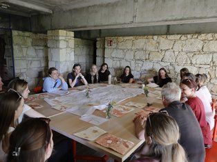 Gruppe von Frauen und Männern sitzt an einem großen Tisch in einem Seminarraum mit Steinwänden.