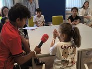 Kinder interviewen sich gegenseitig mit Mikrofon in einem Schulraum in Wien.