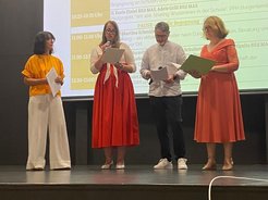 Vier Personen bei einer Veranstaltung in Wien, drei halten Dokumente in der Hand.